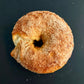 A single cinnamon sugar donut with a bite taken out, resting on a dark black background.
